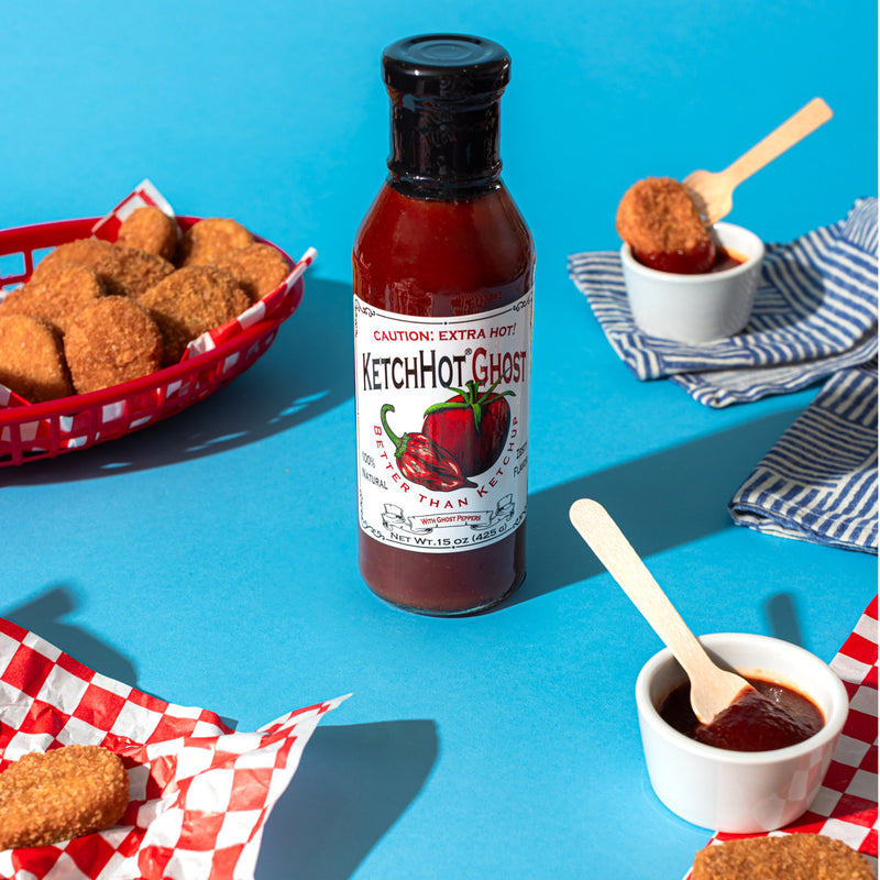 A bottle of KetchHot Ghost on a blue table with chicken nuggets in baskets around it